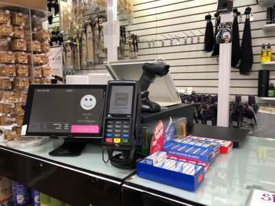 PUREJOIN beauty supply POS system installed at a real beauty supply store checkout counter, featuring a touchscreen register, barcode scanner, and payment terminal.