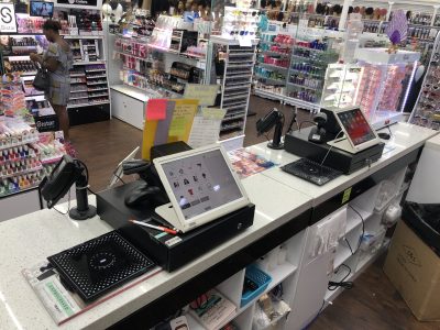 Multiple PUREJOIN beauty supply POS systems installed at a retail checkout counter, featuring touchscreen registers, barcode scanners, and equipment for efficient store operations.