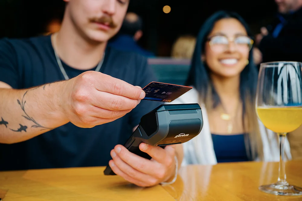 Genius Restaurant POS | PUREJOIN Restaurant Payment Processing Restaurant customer using a Genius payment terminal to make a contactless credit card payment, demonstrating integrated restaurant payments and convenient checkout.